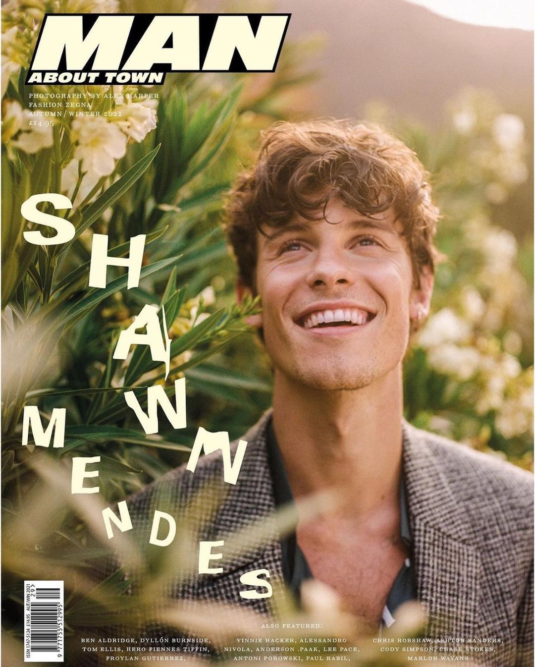 Magazine cover featuring a portrait of Shawn Mendes, smiling and wearing a grey blazer, set against a backdrop of lush green foliage.