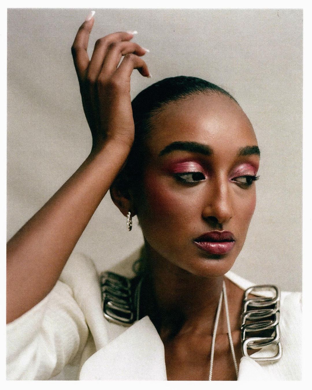 Portrait of a black female model with pink eyeshadow wearing a white jacket with metallic loop details in a photo studio.