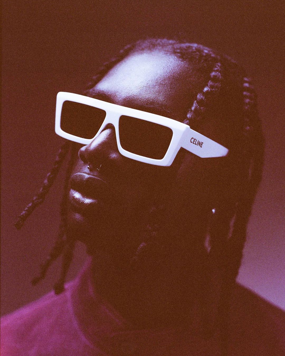 Close-up studio portrait of an African-American adult male wearing white-framed sunglasses with dark lenses against a brown backdrop.