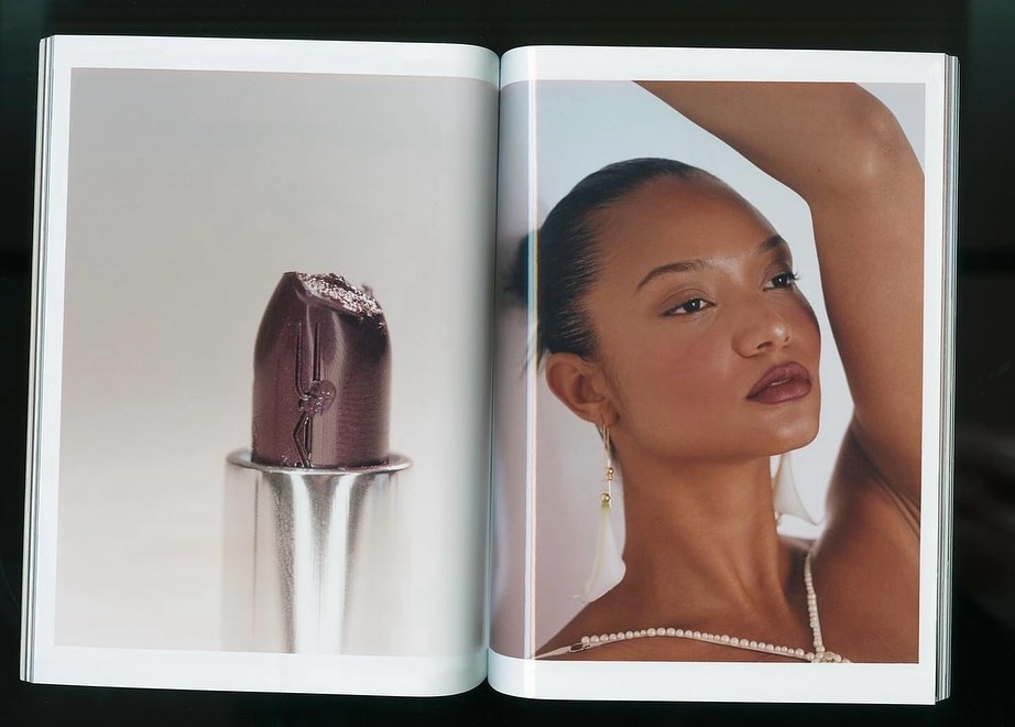 Open magazine spread showing a dark purple lipstick close-up on the left page and a portrait of a woman on the right