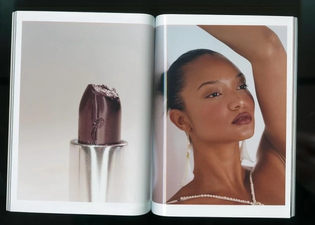 Open magazine spread showing a dark purple lipstick close-up on the left page and a portrait of a woman on the right