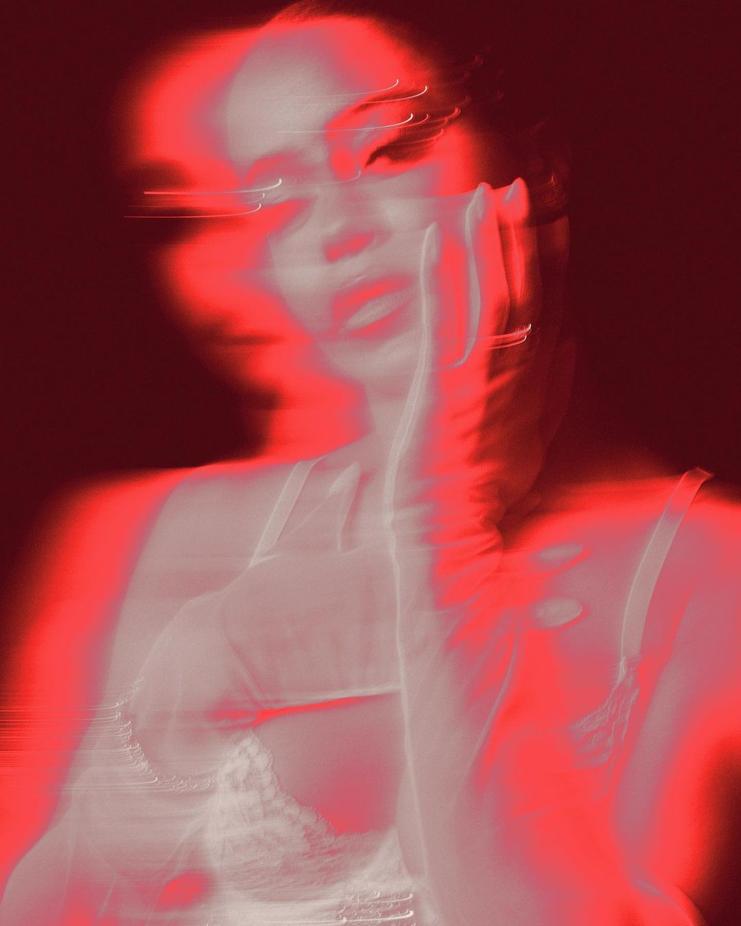 Monochromatic studio portrait of a woman with a hand to her face. The image features a red color grade and blurred motion.