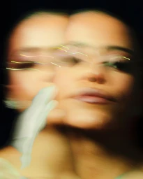 Motion blur portrait of a woman with shimmering eye makeup and a gloved hand near her face against a dark background