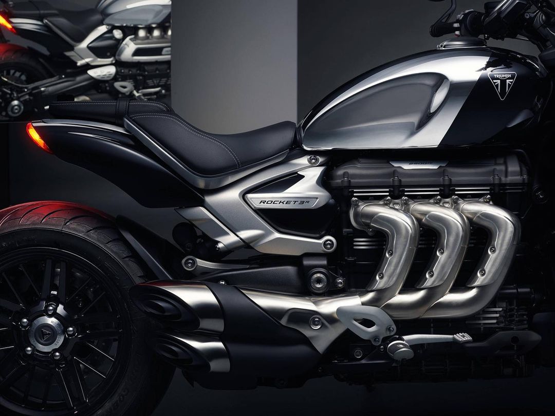 Silver and black Triumph Rocket 3 R motorcycle detail shot in a dark studio with a second bike visible in the background.