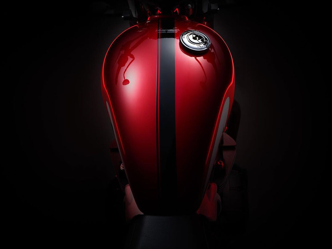 Close-up of a red and black motorcycle fuel tank with chrome cap, reflecting light in a dark, indoor automotive studio.