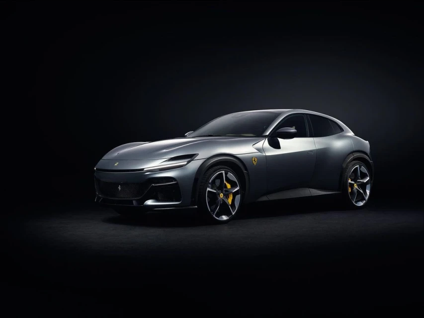 Sleek silver Ferrari Purosangue SUV showcased against a black backdrop, highlighting its sporty design, wheels, and emblem.