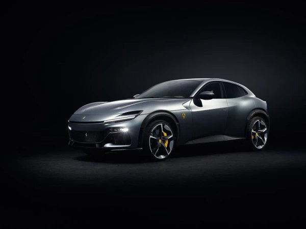 Sleek grey Ferrari Purosangue SUV with yellow brake calipers, illuminated headlights, parked against a stark black backdrop in a studio setting.
