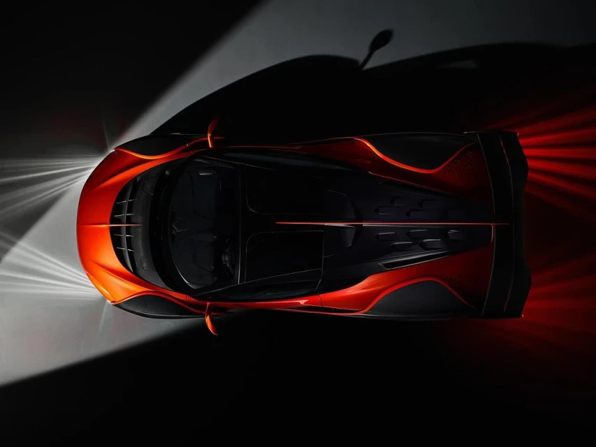 High-angle, close-up of a sleek, orange and black sports car with striking light reflections on its polished surfaces against a dark backdrop.