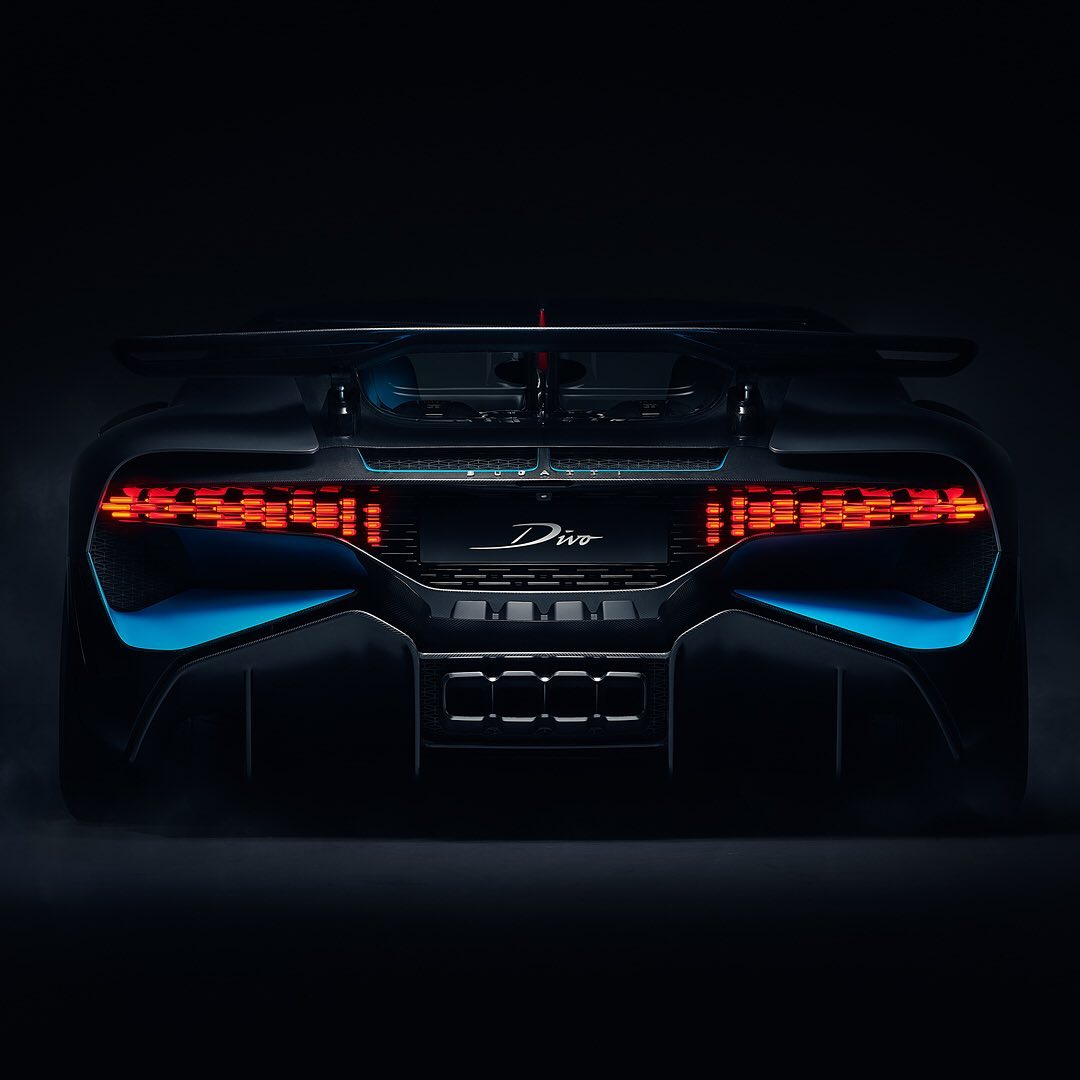 Rear view of a dark blue Bugatti Divo with illuminated tail lights against a dark background in a studio shot, showcasing automotive design.