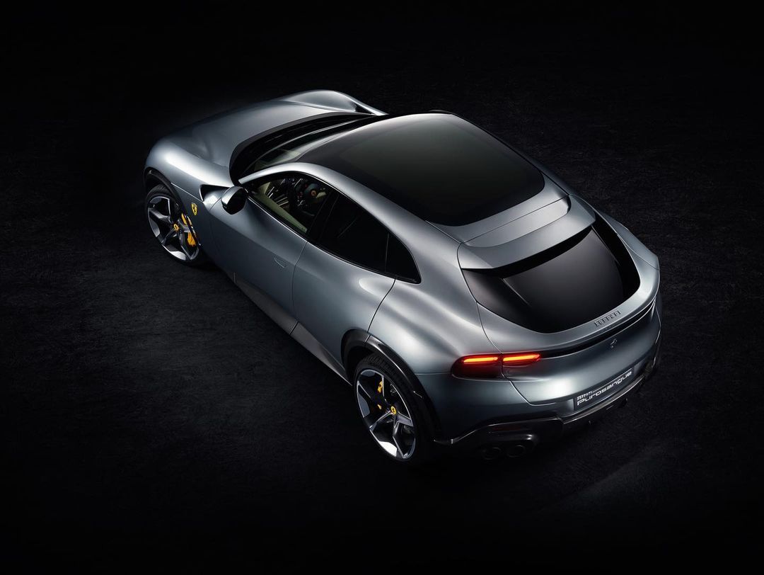 Sleek silver Ferrari Purosangue SUV viewed from above against a black backdrop, showcasing its luxurious design and aerodynamic features.