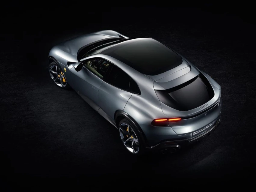 Sleek silver Ferrari Purosangue SUV viewed from above against a black backdrop, showcasing its luxurious design and aerodynamic features.