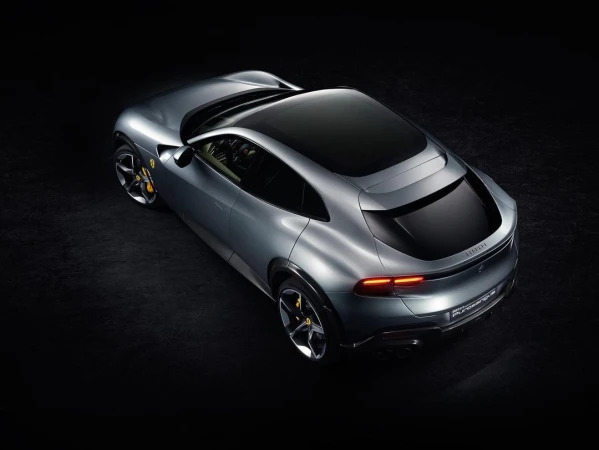 Sleek silver Ferrari Purosangue SUV viewed from above against a black backdrop, showcasing its luxurious design and aerodynamic features.