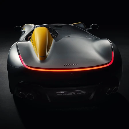 Rear view of a gray and yellow Ferrari Monza SP1 sports car against a black background showcasing its sleek design and taillights.