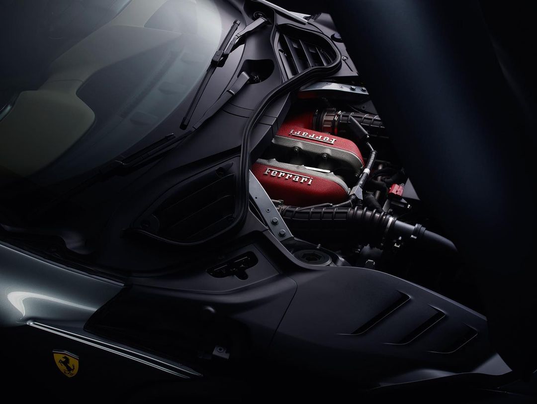 Exposed red Ferrari engine under the hood, showcasing the car's internal mechanics and design in a dark and moody setting.