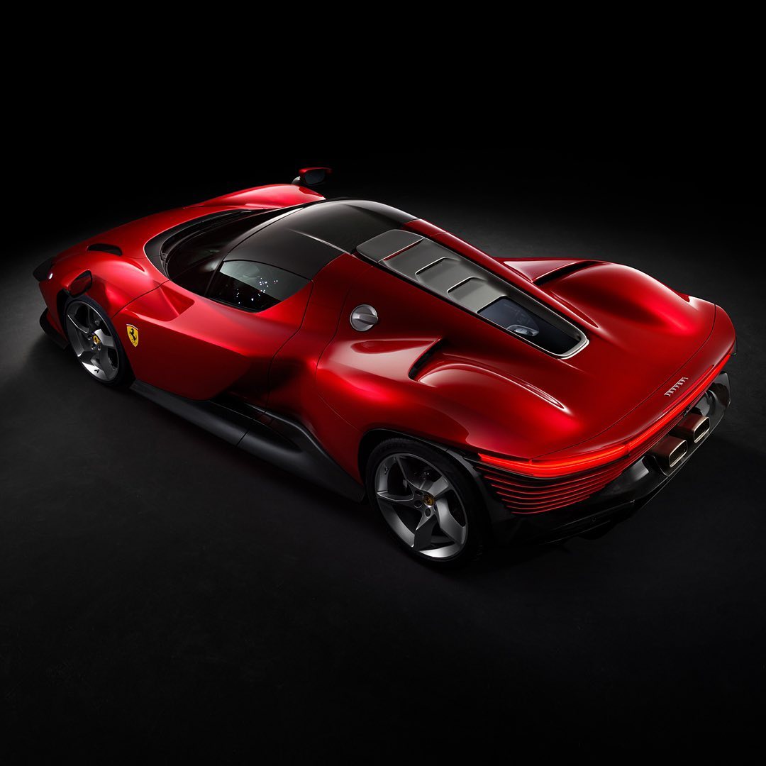 Red Ferrari Daytona SP3 showcasing sleek lines, aerodynamic design, and rear engine visible on a black background in a studio shot.