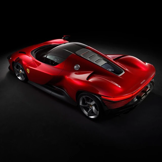 Red Ferrari Daytona SP3 showcasing sleek lines, aerodynamic design, and rear engine visible on a black background in a studio shot.