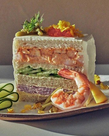 A culinary creation: a multi-layered sandwich with shrimp, cucumber, and ham, presented on a decorative plate, a gastronomic work of art.