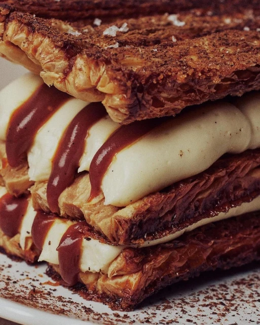 Eye-level, close-up shot of a layered mille-feuille pastry with cream filling and caramel drizzle, showcasing textures and inviting food photography.