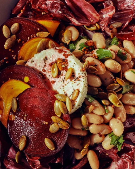 Overhead shot of a vibrant salad featuring red and golden beets, goat cheese, white beans, pumpkin seeds, and red cabbage, showcasing a fresh and colorful dish.