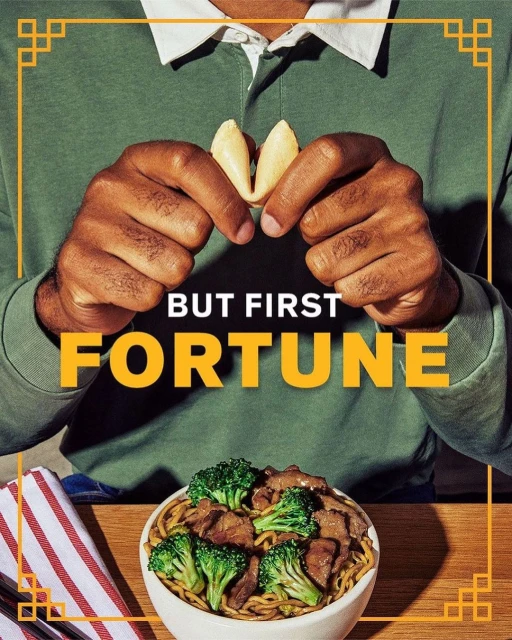 Person holds fortune cookies over noodles with beef and broccoli, next to a red striped towel, promoting Chinese cuisine.