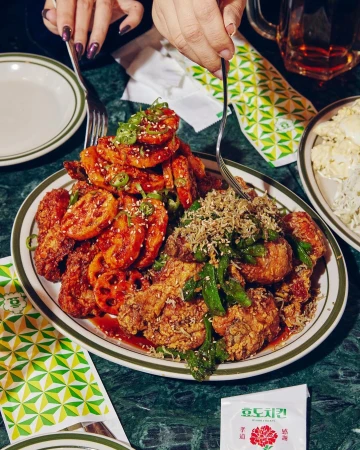 Overhead shot of an oval plate piled high with Korean fried chicken and lotus root, set on a green marble table with patterned napkins.
