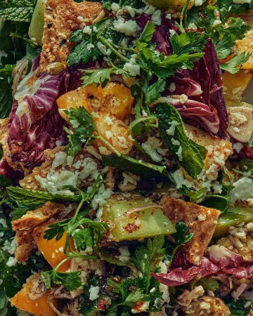 Overhead shot of a vibrant salad with mixed greens, herbs, toasted grains, cheese crumbles, and fruit chunks, creating a visually appealing dish.