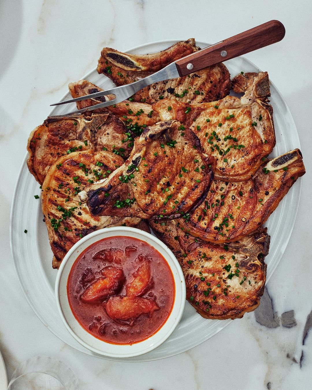Overhead shot of grilled pork chops with a brown sauce and a serving fork on a white plate, creating an inviting food presentation.