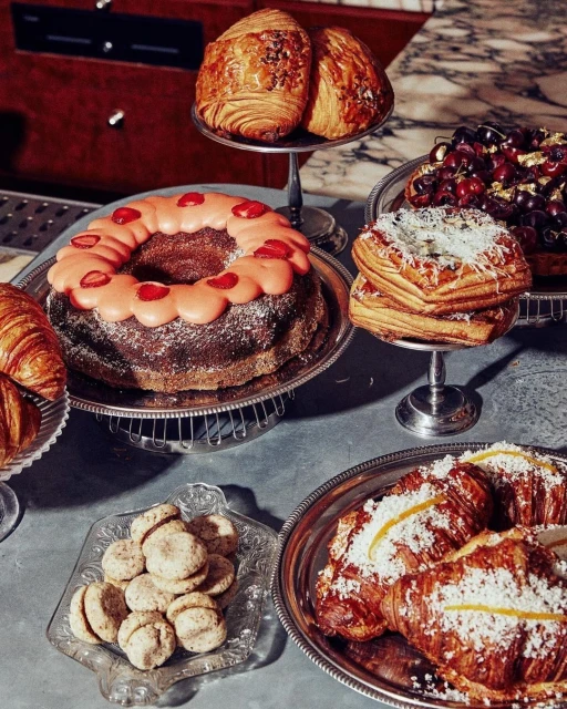 A delicious display of pastries, including croissants, cake, and cookies, arranged on silver platters atop a gray marble surface.