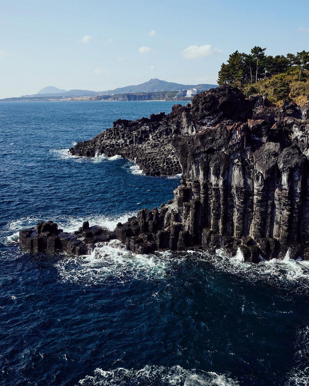 Scenic view of a rocky coastline with columnar basalt formations meeting the blue ocean under a clear sky, showcasing natural beauty.