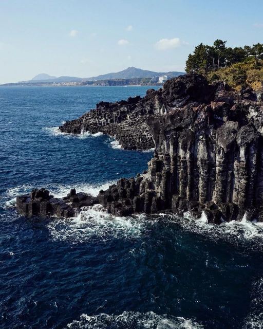 Scenic view of a rocky coastline with columnar basalt formations meeting the blue ocean under a clear sky, showcasing natural beauty.