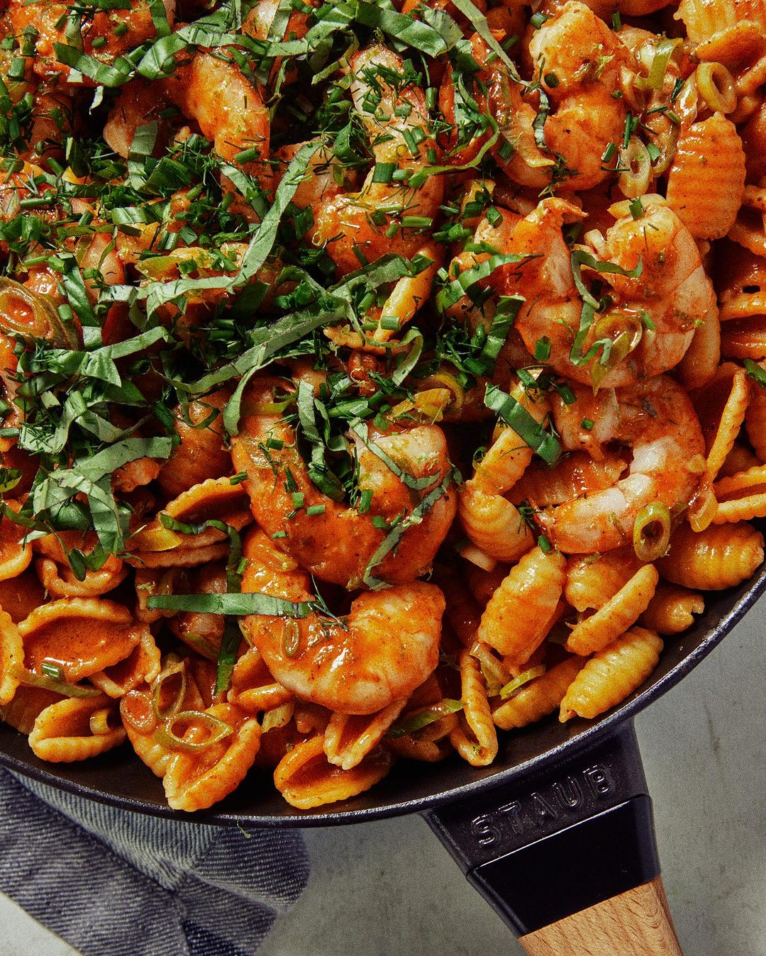 Overhead shot of shrimp pasta with sauce, green onions, and basil served in a black pan. Delicious seafood, Italian cuisine dish.