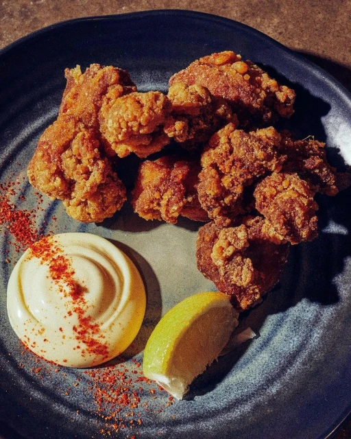 Close-up of crispy fried chicken pieces on a plate with a creamy sauce and a lime wedge, creating an appetizing food still life.