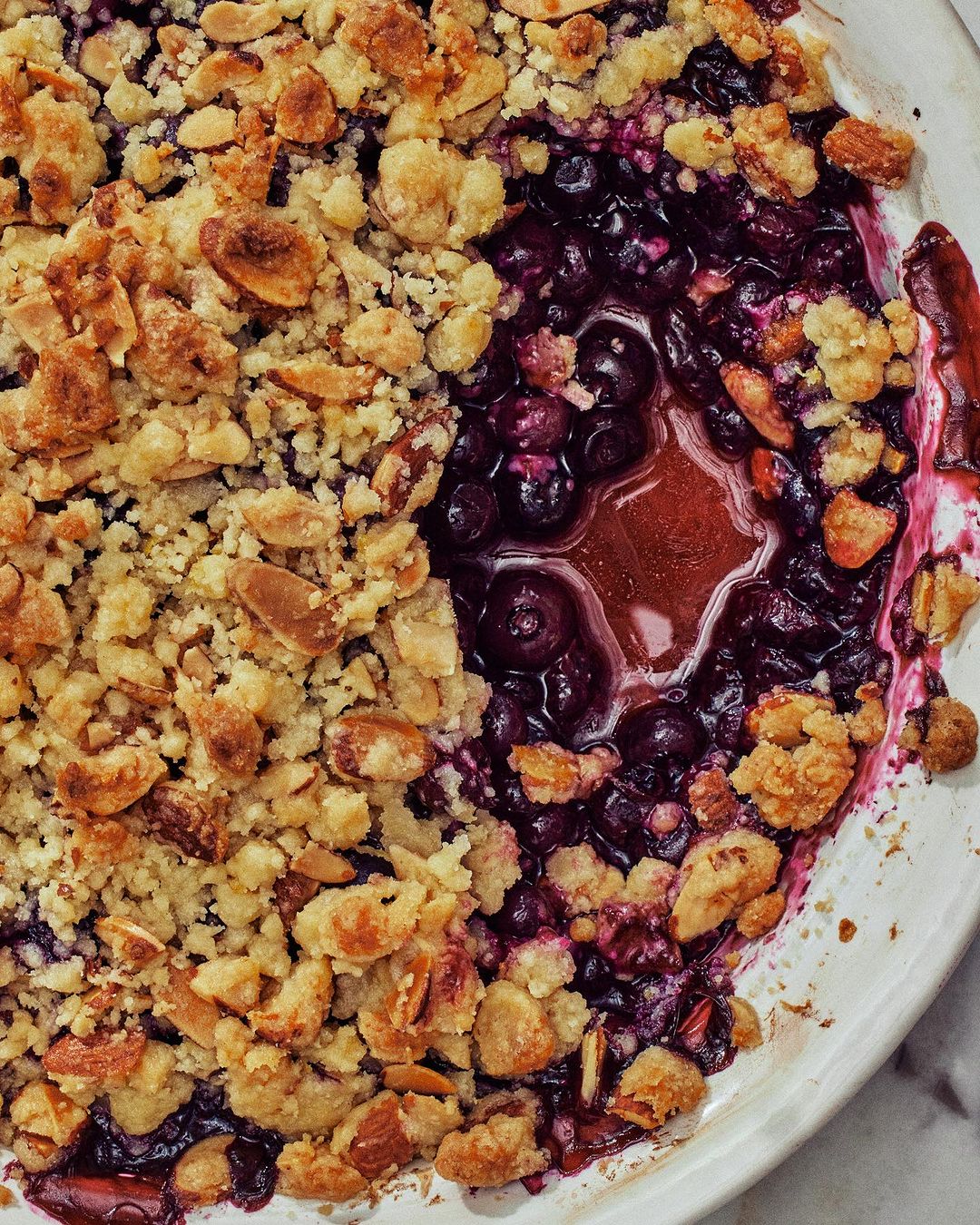 Overhead shot of a delectable blueberry crumble dessert in a white dish, showcasing a golden brown crumble topping and juicy filling.