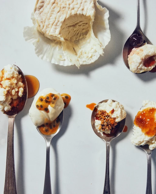 Overhead studio shot of a gourmet cheese block and spoons of desserts with fruit toppings, set against a bright white backdrop.