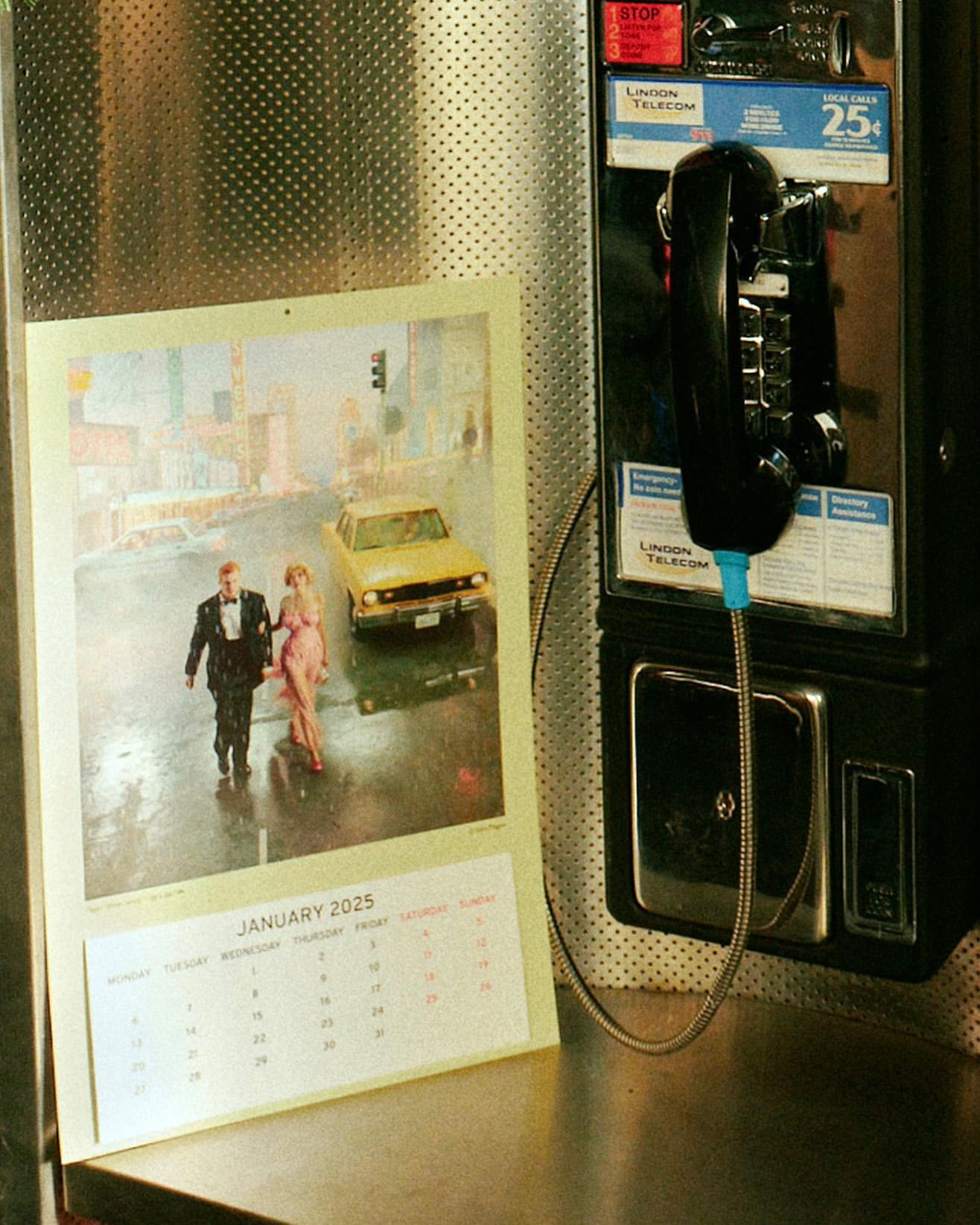 Calendar photo shows an elegantly dressed couple walking in the rain with a yellow car and buildings in the background, hanging next to a payphone.