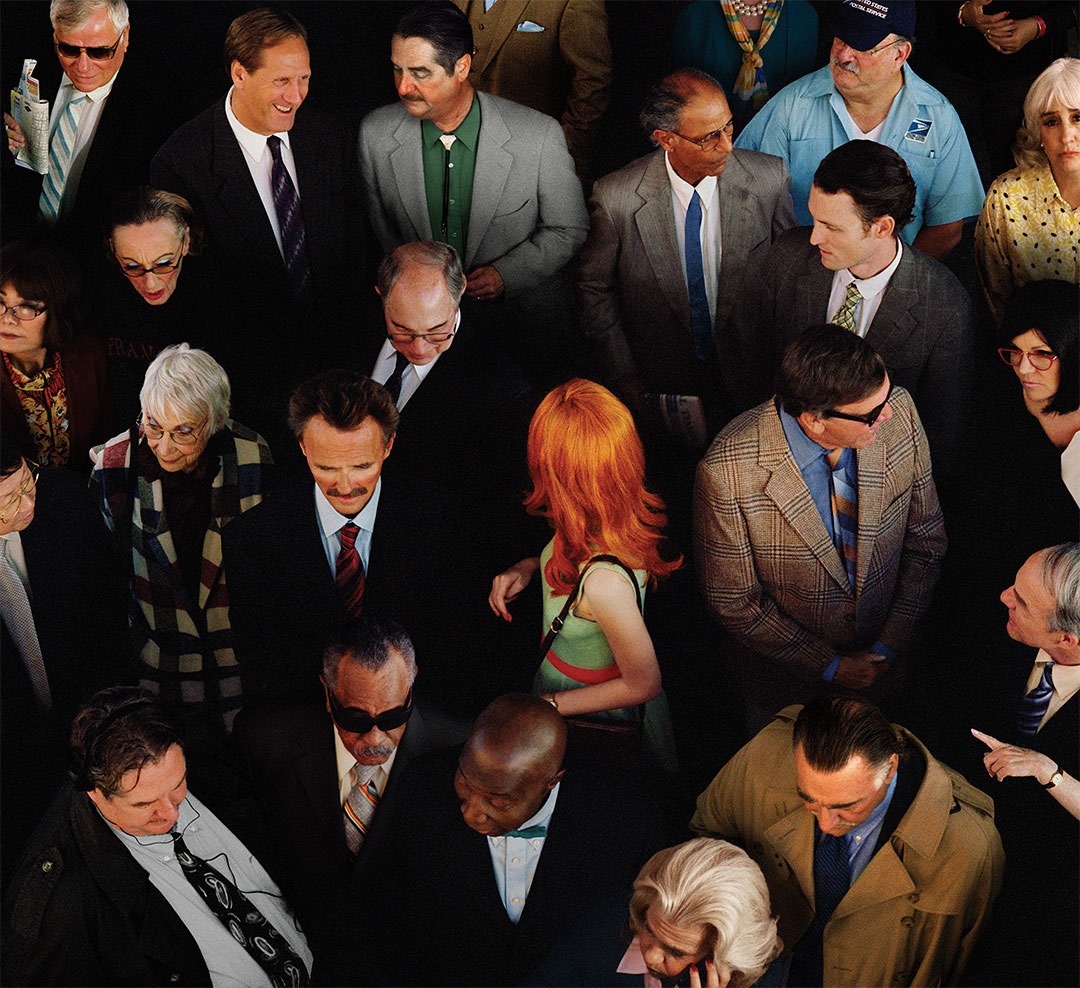 Overhead shot of a diverse crowd of people in suits and business casual attire, including one woman with red hair, filling the frame.