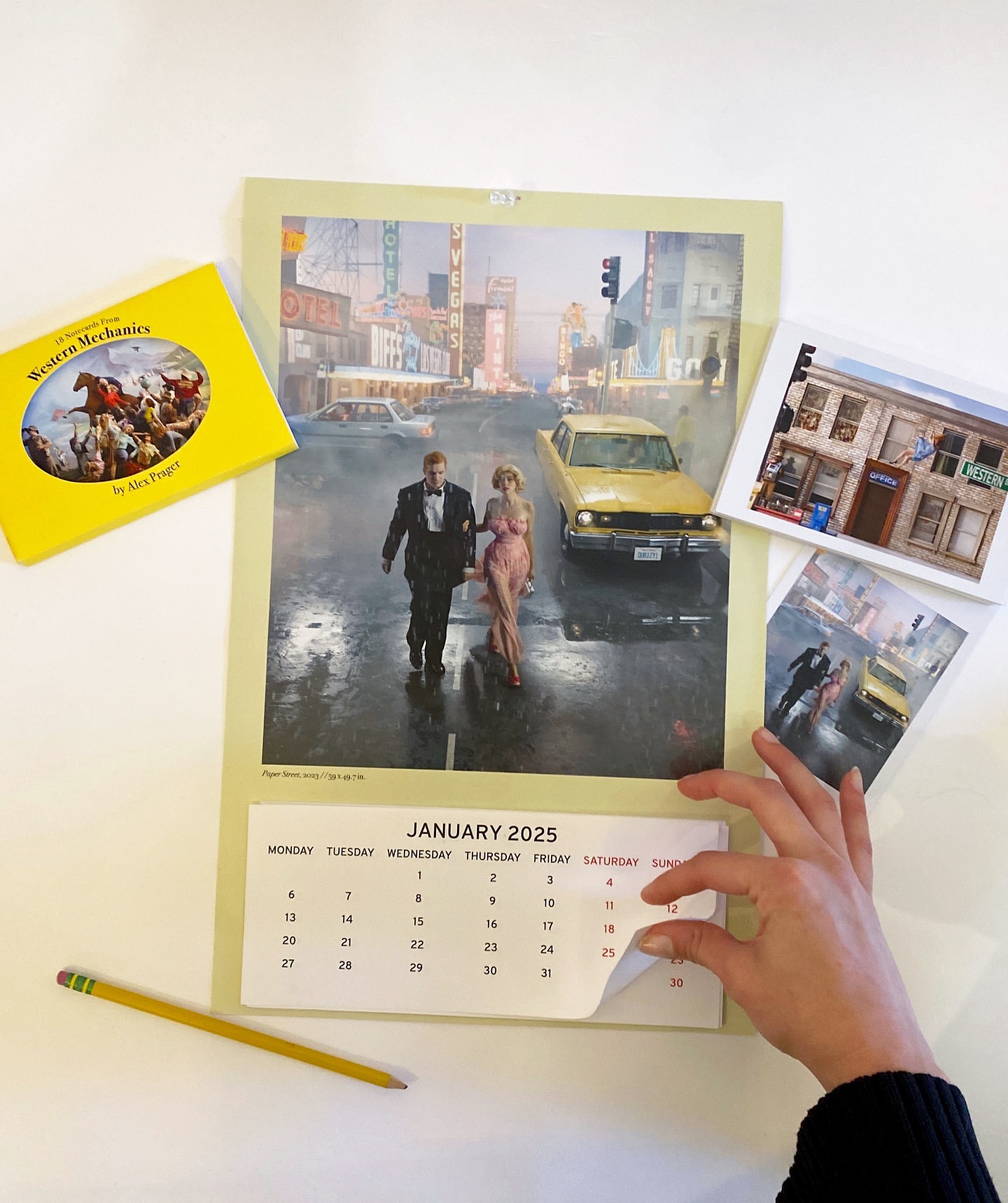 Calendar page featuring an illustration of a couple walking in a city street, a book, and a postcard on a white surface.