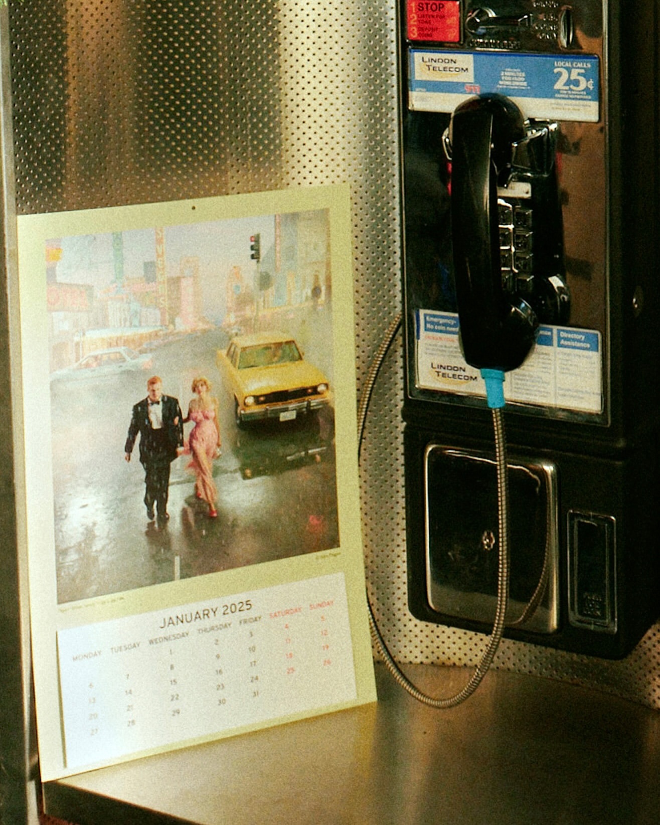 Pay phone with calendar showing January 2025 featuring an illustration of a couple and a yellow car on a wet city street.