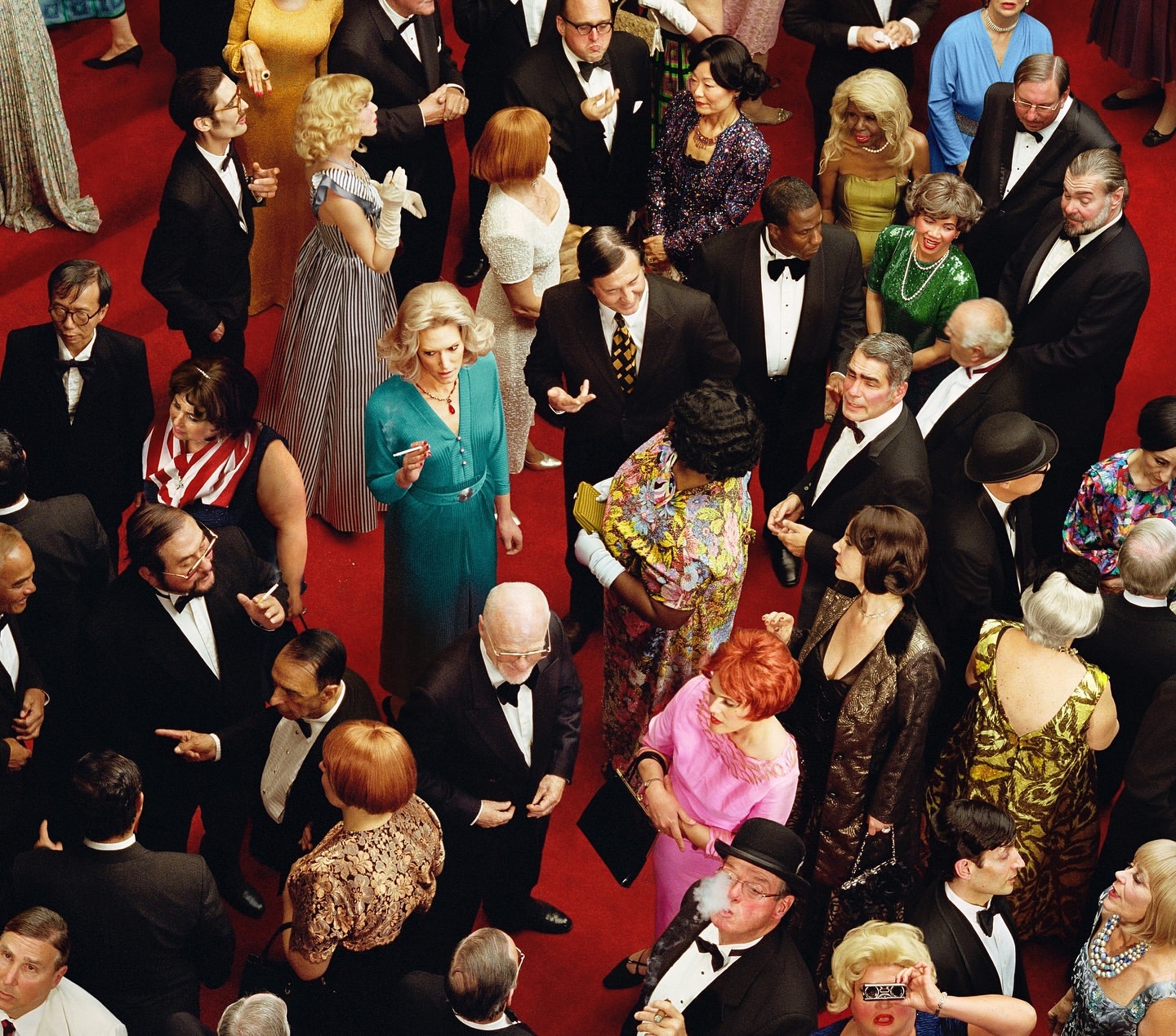 Overhead shot of a large crowd dressed in formal wear on a red carpet, many wearing tuxedos and gowns, at a formal event.