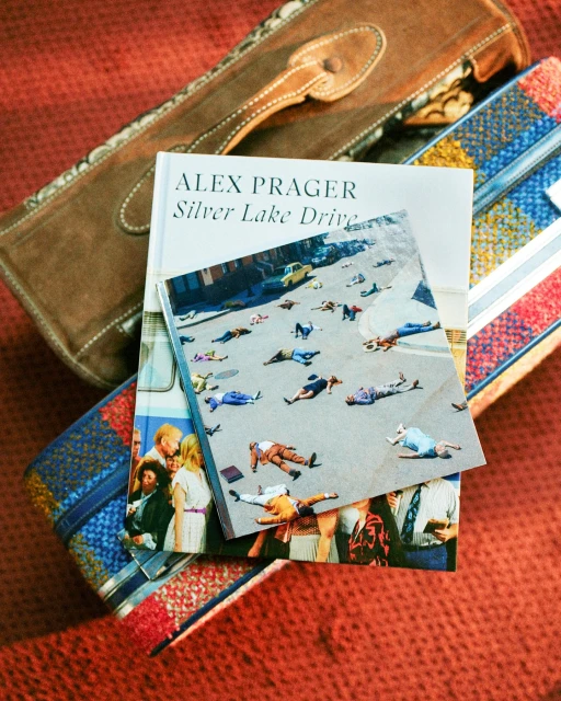 Book cover of 'Silver Lake Drive' by Alex Prager placed on patterned fabric with brown handbag. Featuring photograph of people lying on street.