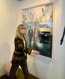 Woman in brown plaid blazer walking past a large framed photographic print hanging on a white wall