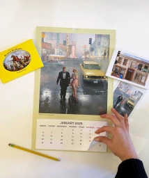 A person turning the page of a January 2025 calendar featuring a cinematic street scene with a yellow car, alongside a yellow book and photos