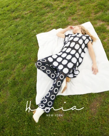 Woman in black and white patterned outfit lies on a white blanket on a green lawn, eyes closed in outdoor fashion shot.