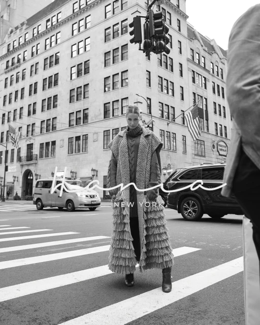 Editorial fashion shot of a woman wearing a long fringe coat in a monochrome urban environment on a crosswalk in New York City.