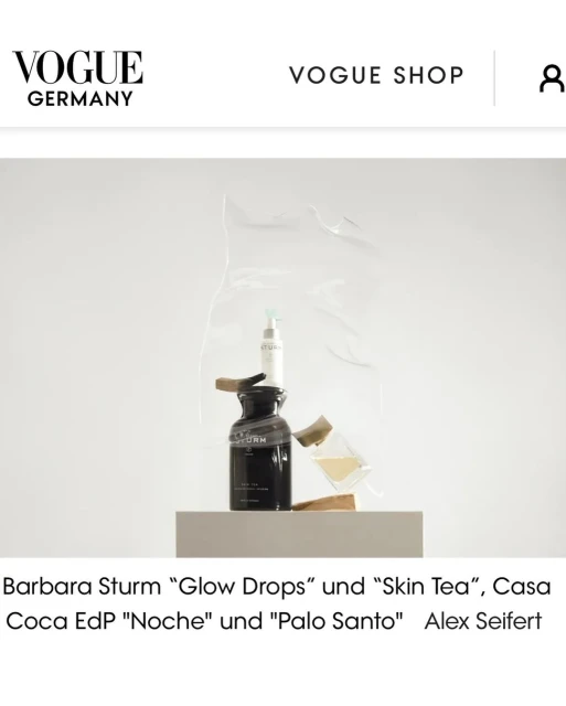 Cosmetic products, including a serum and a bottle of lotion, are displayed on a platform against a white backdrop with "Vogue Germany" text.