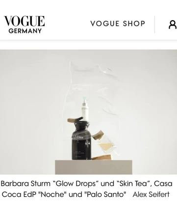 Cosmetic products, including a serum and a bottle of lotion, are displayed on a platform against a white backdrop with "Vogue Germany" text.