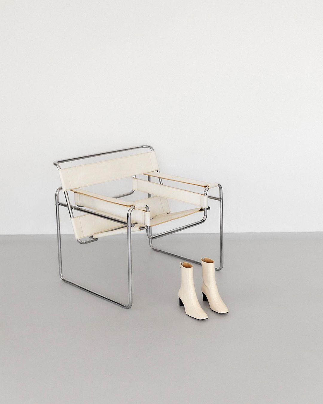 Minimalist composition with a Bauhaus-style Wassily chair, and a pair of ankle boots against a clean, neutral background.