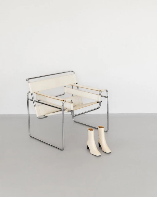 Minimalist composition with a Bauhaus-style Wassily chair, and a pair of ankle boots against a clean, neutral background.