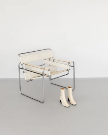 Minimalist composition with a Bauhaus-style Wassily chair, and a pair of ankle boots against a clean, neutral background.