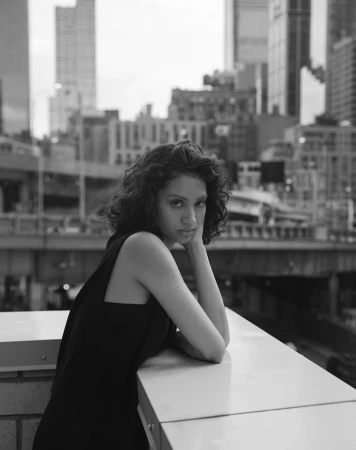 Monochrome portrait of a woman resting her chin on her hand against an urban rooftop and city skyline background.